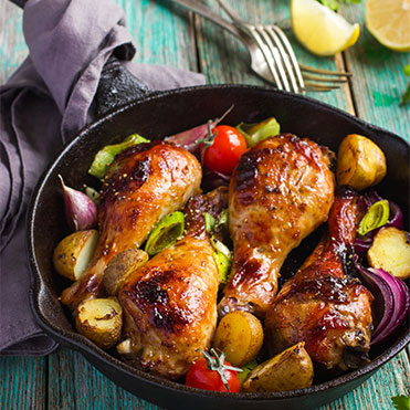 Cast-iron skillet filled with roasted chicken and vegetables sitting on rustic blue table