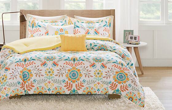 A bright and colorful patterned bedspread with yellow and blue floral medallions and bird motifs on it. 