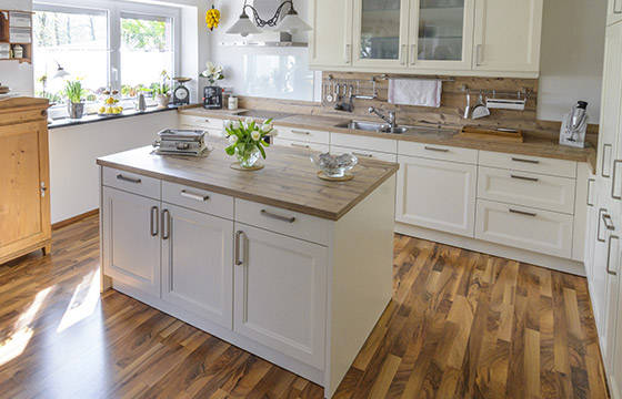An open an airy kitchen with white cabinets, and a light walnut wood flooring. 