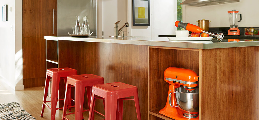 A galley kitchen with coral red metal bar stools tucked under the kitchen counter. 
