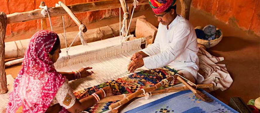 Two people from India weaving a rug on a loom