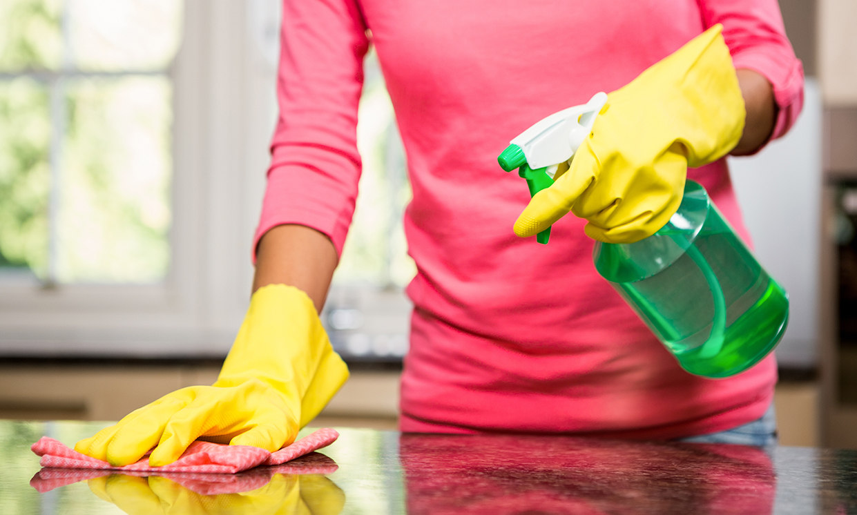 Close up of woman wearing yellow gloves using cleaner and wiping down her kitchen counter