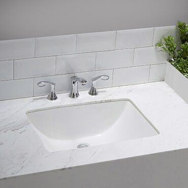 Close up of white poreclin sink set in marble countertop with a silver faucet