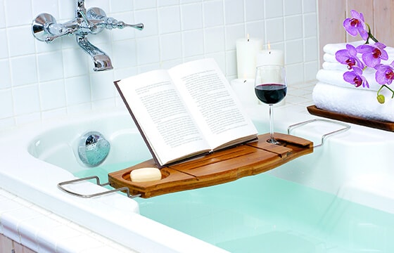 Bath tub caddie in a bath tub with book candles, and wine