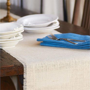 Cream burlap table runner with blue napkins on brown table, set with plates