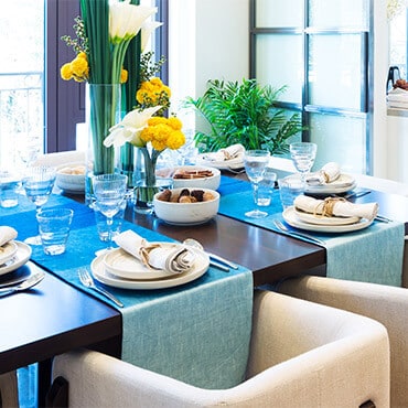 Dining room table set with two blue table runners, tableware, and centerpiece