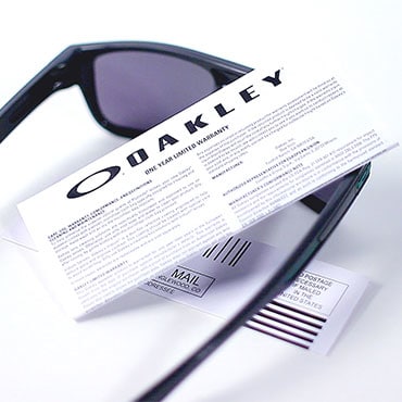 A pair of black Oakley sunglasses with a certificate of authenticity laying on top of the sunglasses