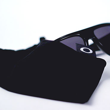 A pair of black Oakley sunglasses laying next to velvet sunglass pouch