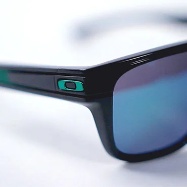 A pair of black Oakley sunglasses, focusing on the Oakley logo on the side of the frame