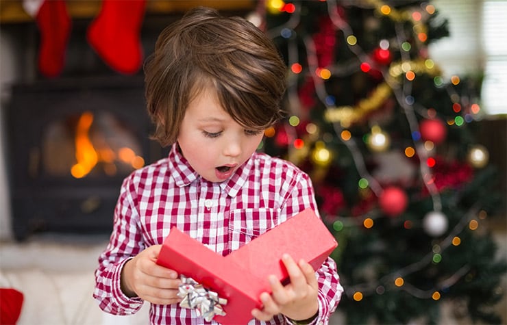 Young boy opening present with stocking stuffer ideas including blu-ray, jewelry, and toy car