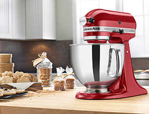 Red Kitchen Aid mixer on a kitchen counter with lots of sugar cookies next to it