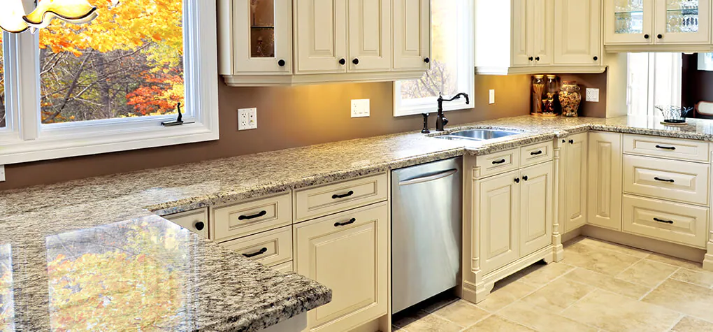 Light kitchen with off white cabinets and light granite countertops shown with stainless steel dishwasher.
